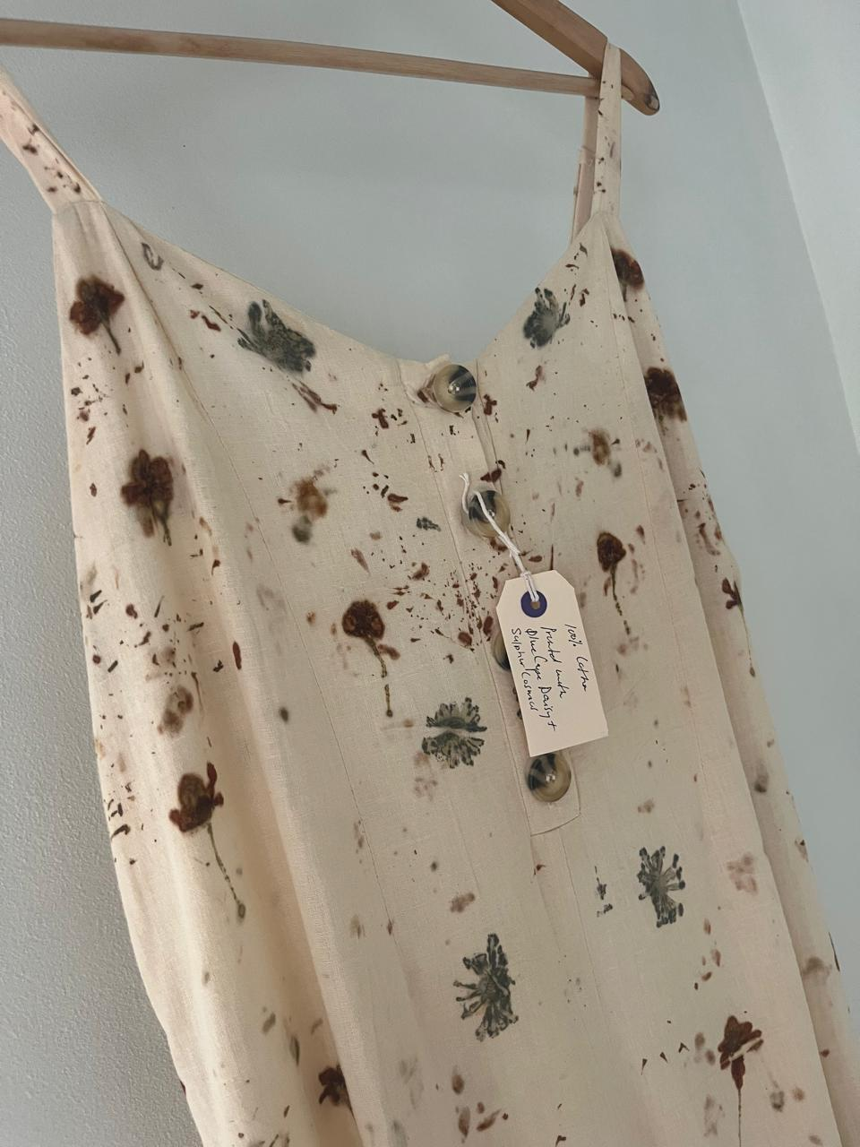Close-up of a botanical printed cotton dress showing leaf prints, horn buttons and a hand-written KAIA tag