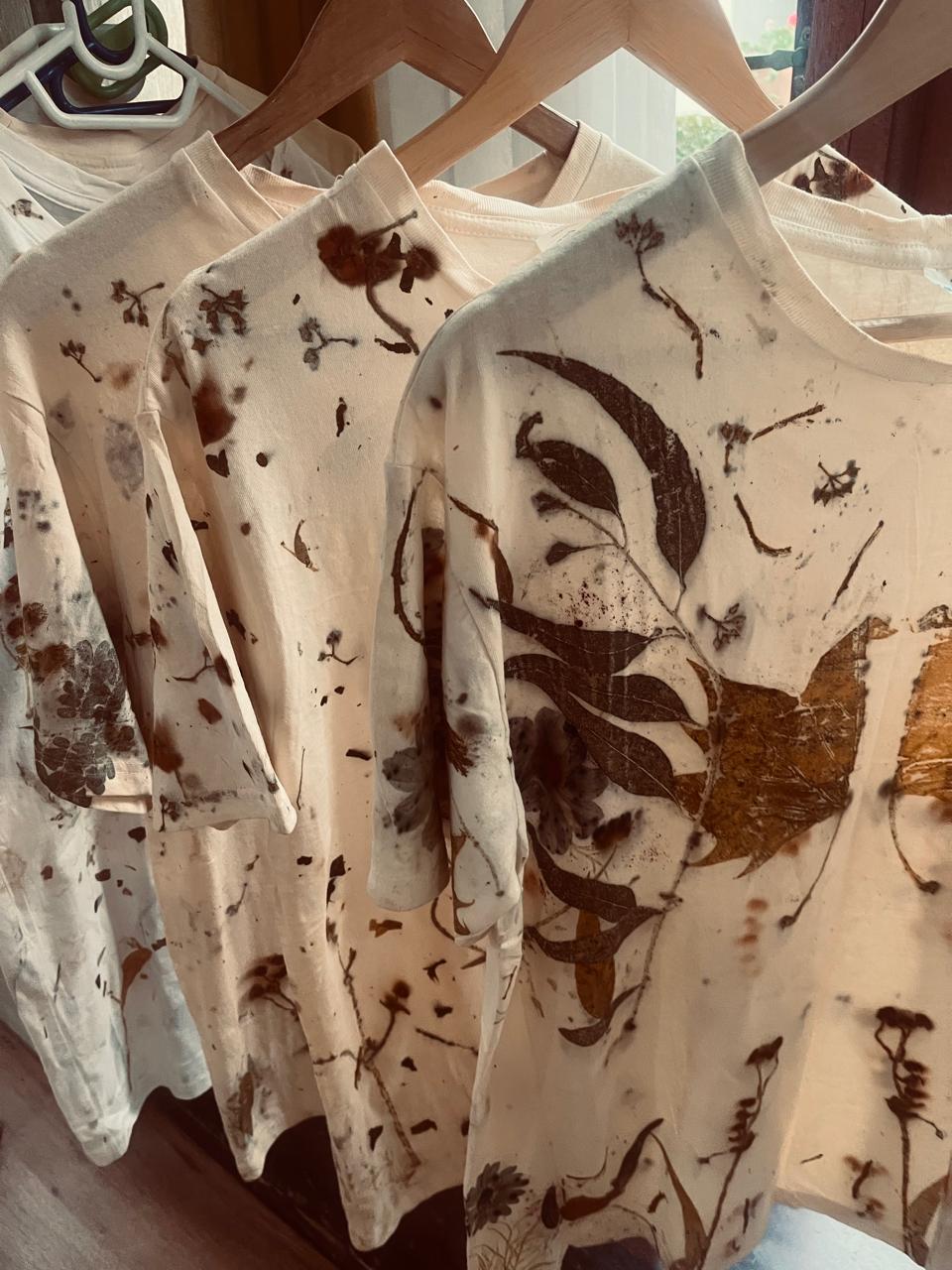 Botanical eco-printed cotton tops hanging on wooden hangers in the studio window light
