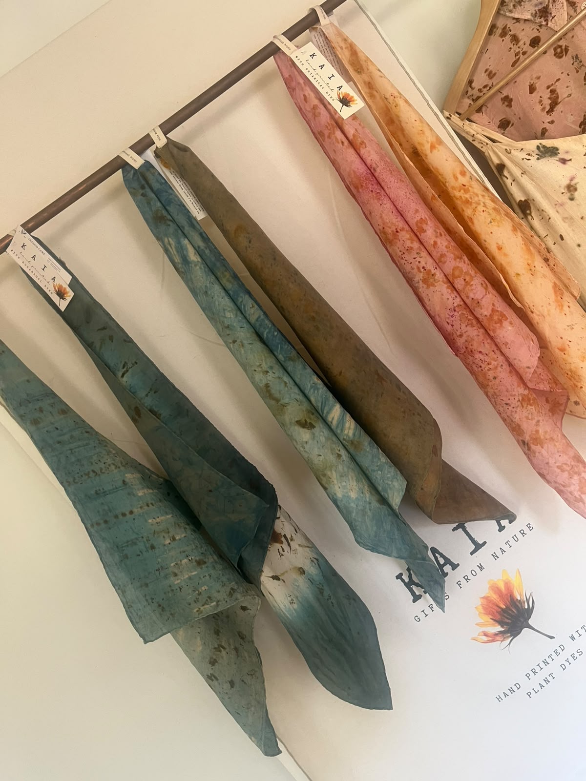 KAIA scarves in blue, green, pink and orange hanging from a copper rail