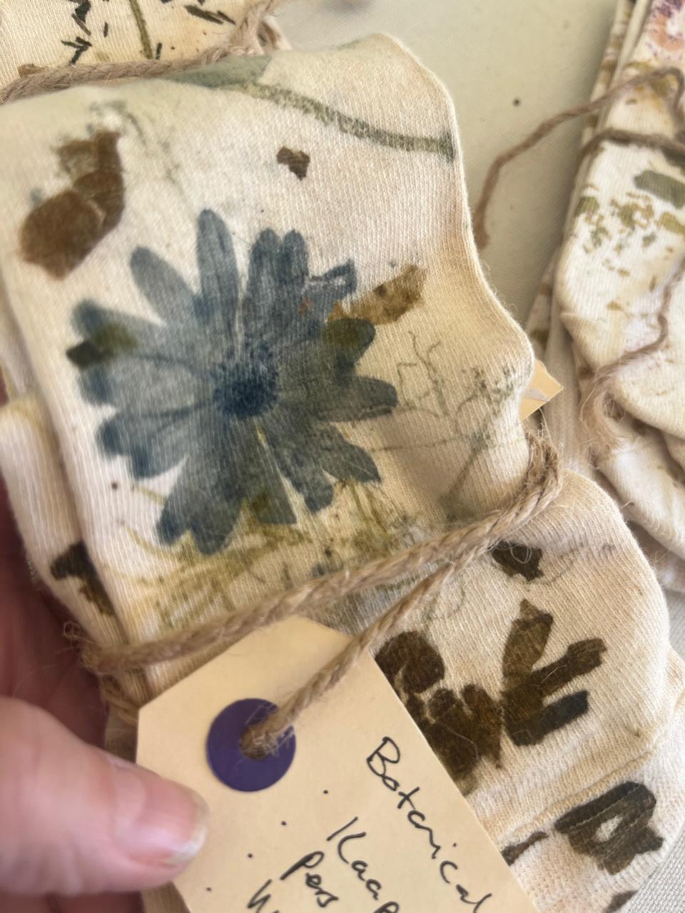 A hand holding folded botanical-printed cloth with a blue daisy print and handwritten tag