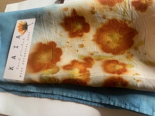 A marigold botanical printed cloth resting on indigo-dyed fabric with its KAIA tag