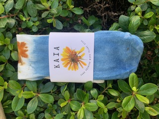KAIA eco-printed socks in indigo and marigold with their tag, resting on green foliage