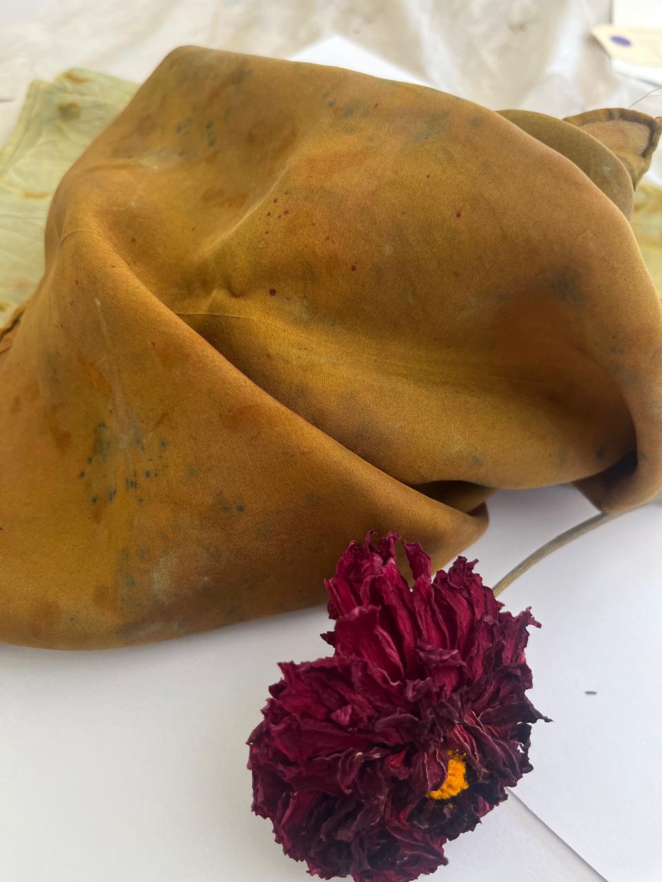 An ochre plant-dyed silk scarf draped beside a dried burgundy flower