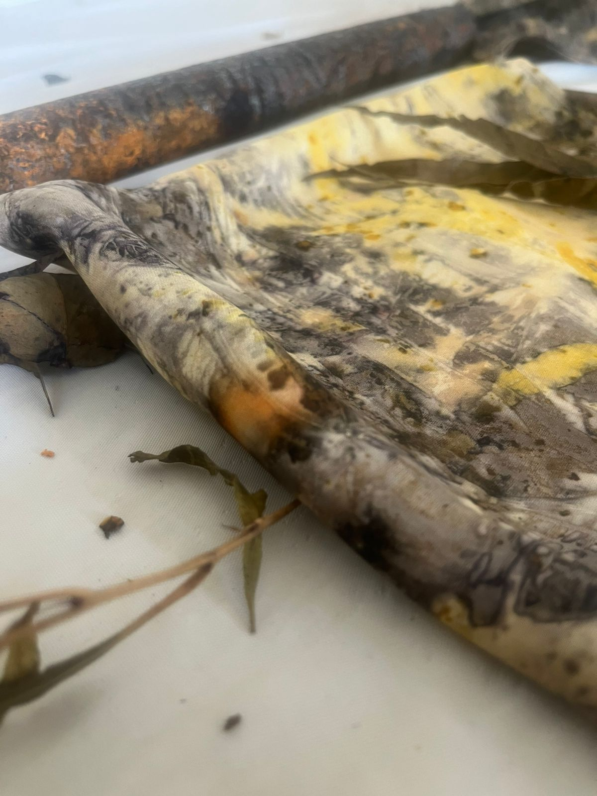 A botanical printed silk in soft yellow and grey leaf marks, unrolled from a rusted pipe