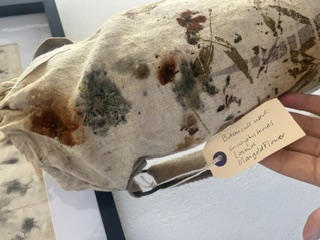 Close-up of a botanical printed yoga bag with grey and rust flower marks and its hand-written tag
