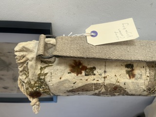 A botanical printed yoga mat bag with its hand-written KAIA tag, standing against a framed print