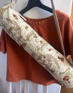 A botanical printed yoga mat bag with a natural cotton strap, carried over a rust coloured top