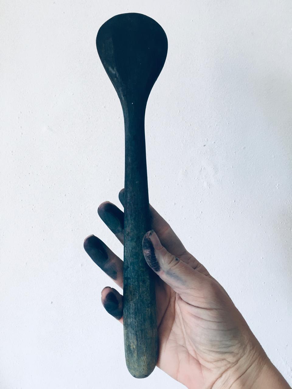 An indigo-stained hand holding the wooden stirring paddle from the vat