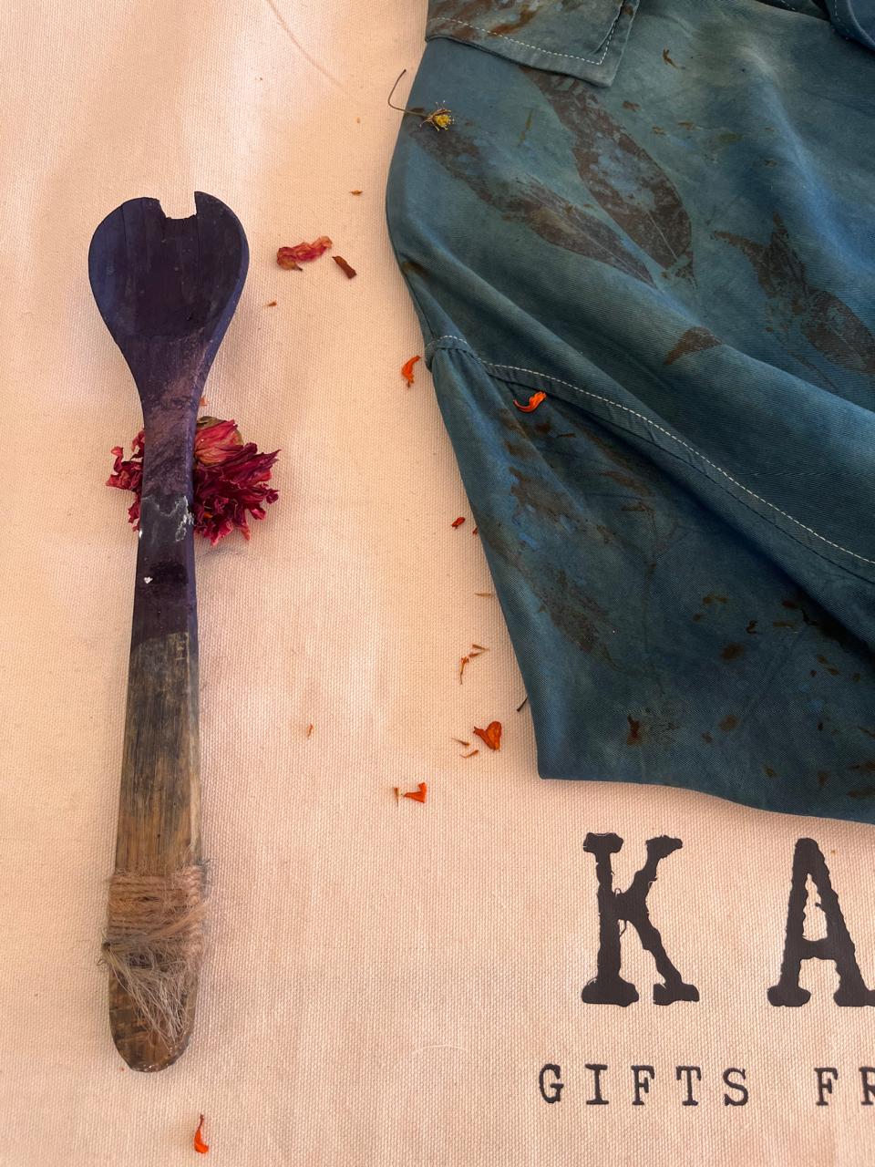 An indigo dyed botanical printed shirt resting on the KAIA cloth beside a dye paddle