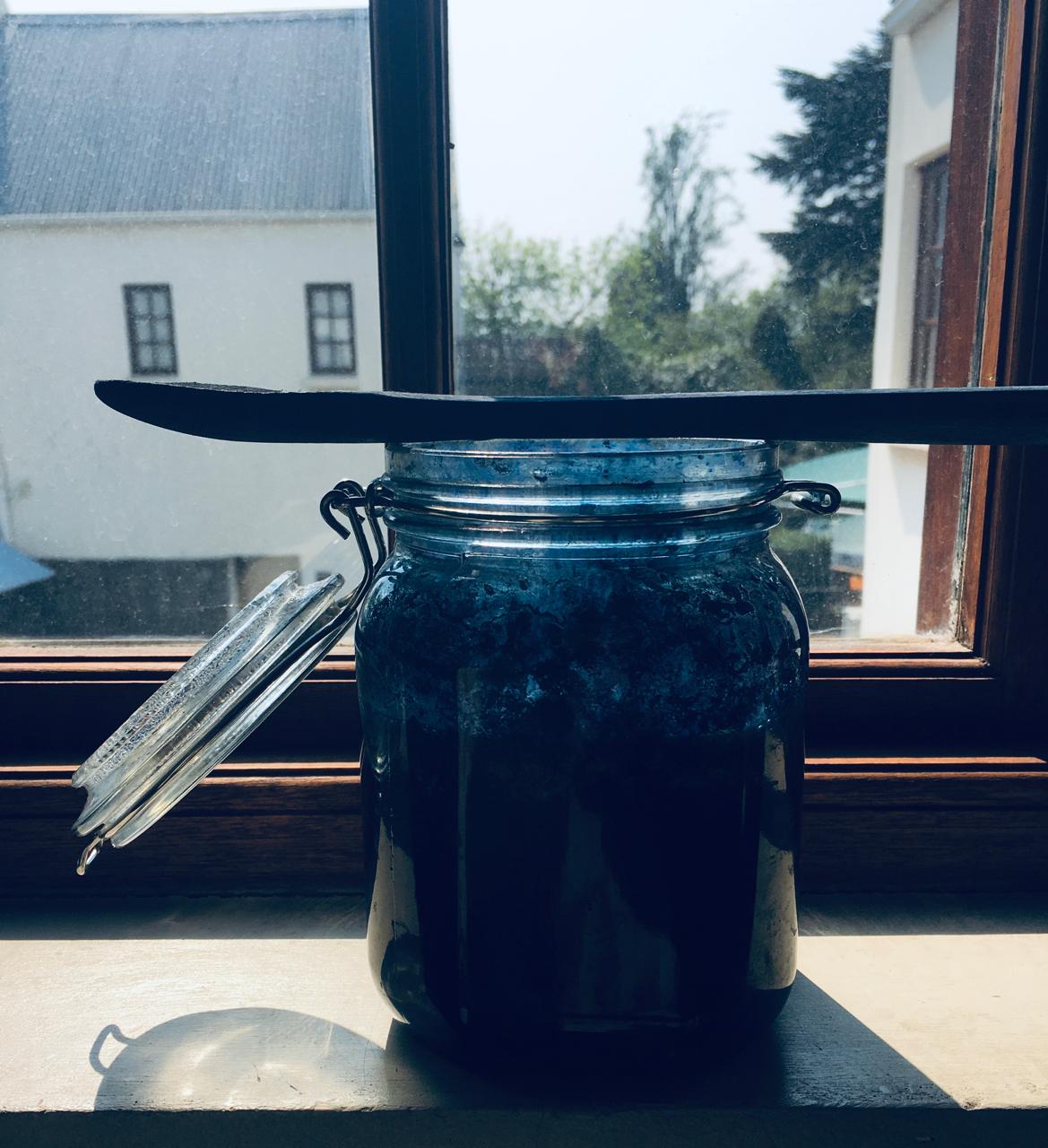 A glass jar of living indigo vat catching the light on the studio window sill