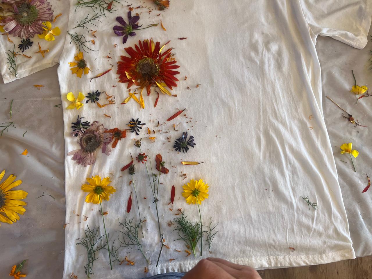 Flowers and botanical material laid out across a white cotton T-shirt