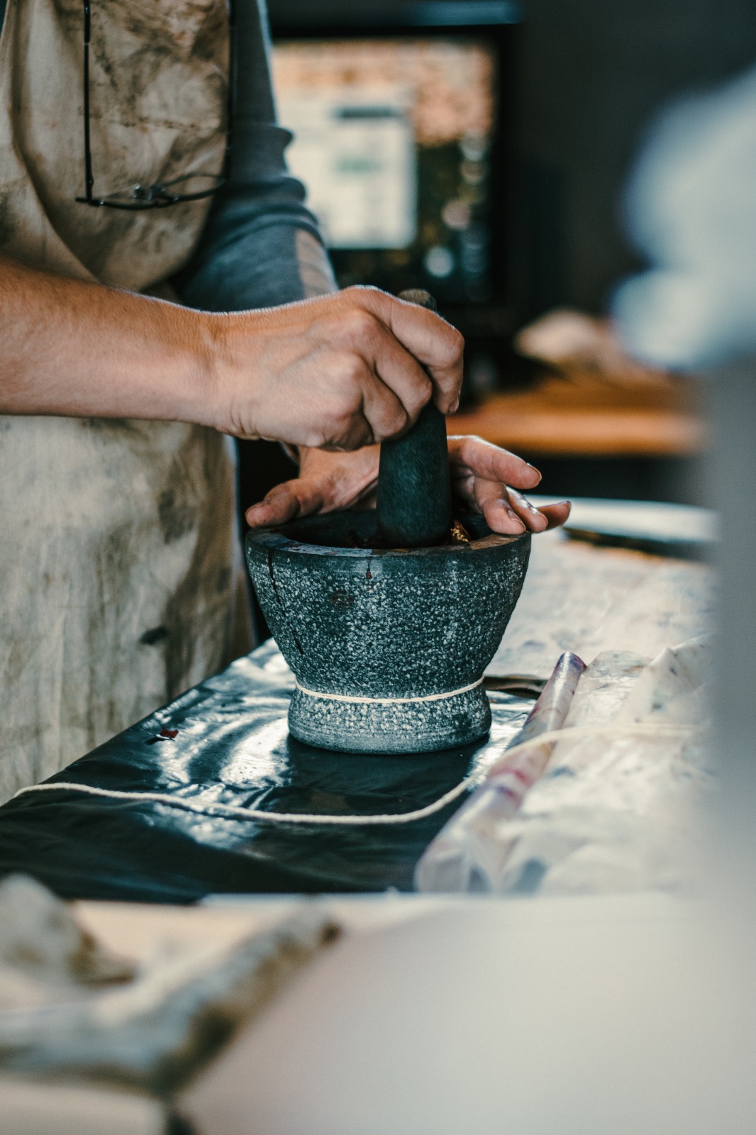 Hands grinding botanical material with a stone mortar and pestle in the studio