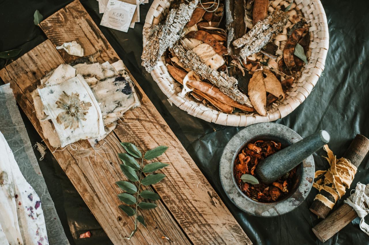 Overhead view of bark, seed pods, printed cloth samples and a mortar on the studio table