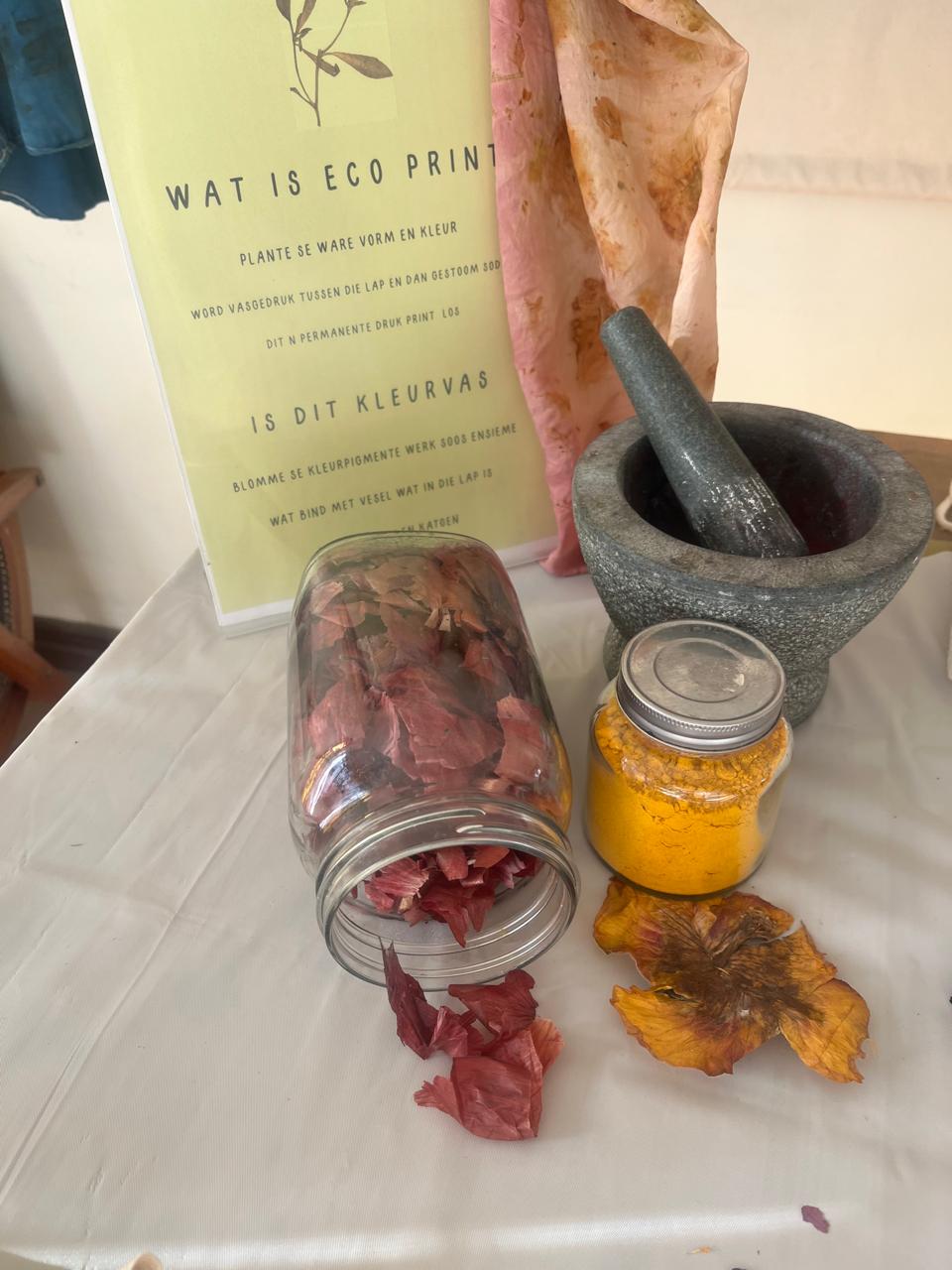 Glass jars of dried hibiscus and turmeric pigment beside a mortar and eco-print display